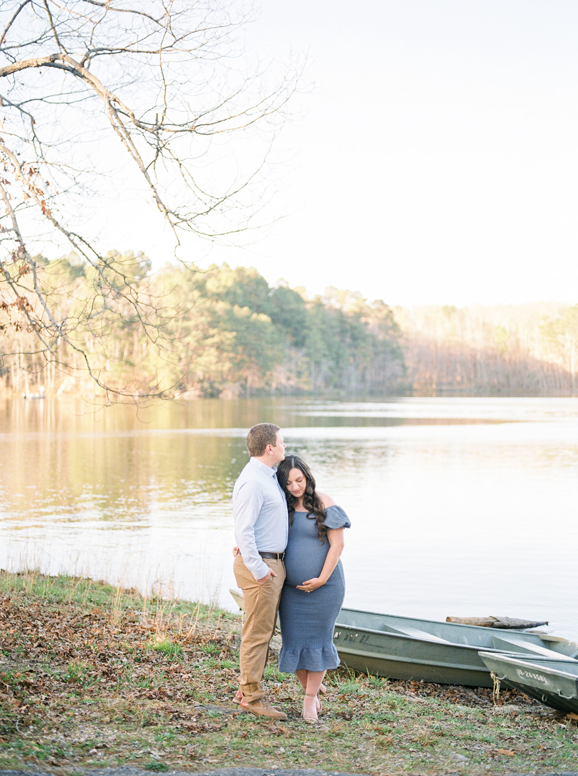 Husband and wife embrace in front of DeKalb County Lake during intimate maternity photography session