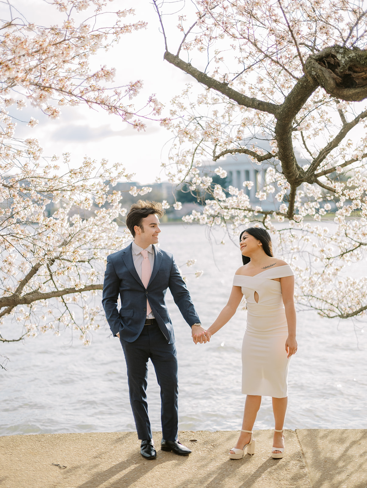 An engaged couple holding hands in front of peak-bloom cherry blossom trees in Washington DC.