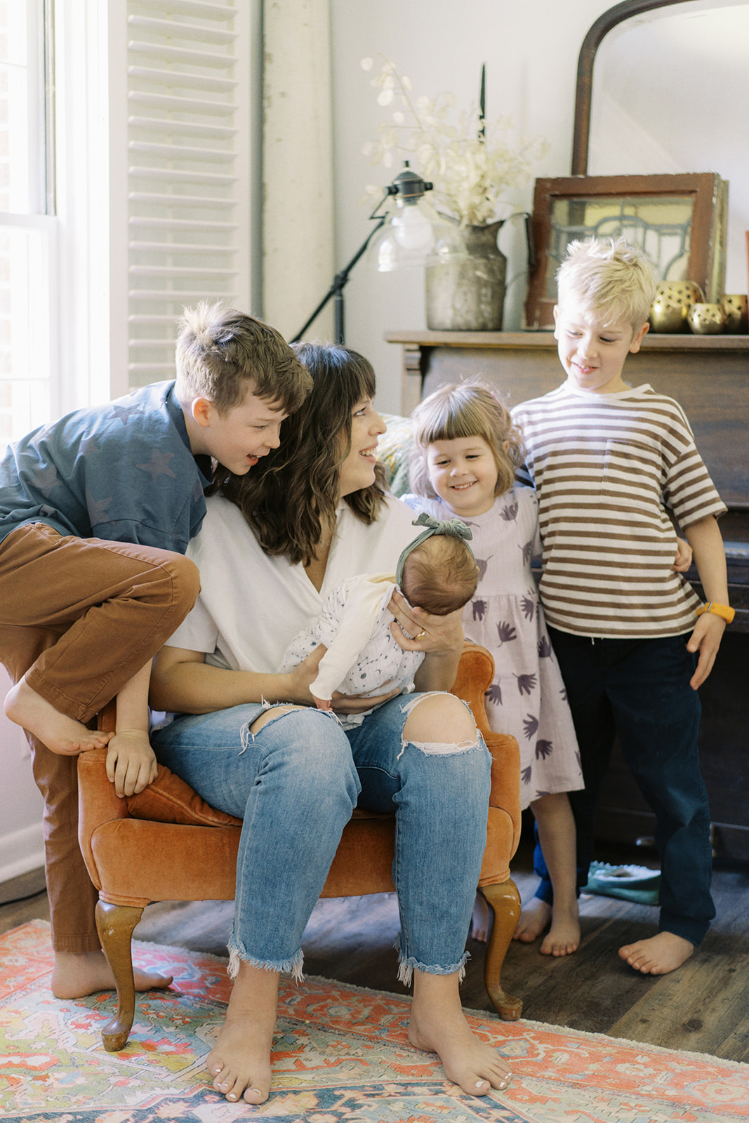 Brothers and sisters smile with mom at the new baby during an at-home lifestyle session