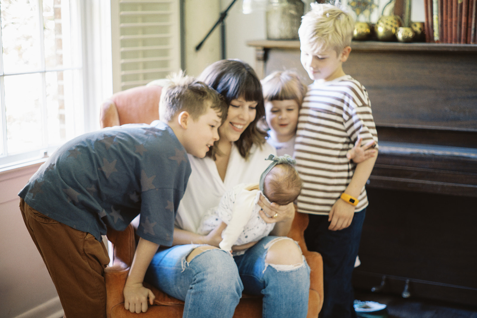 Brothers and sisters smile with mom at the new baby during an at-home lifestyle session