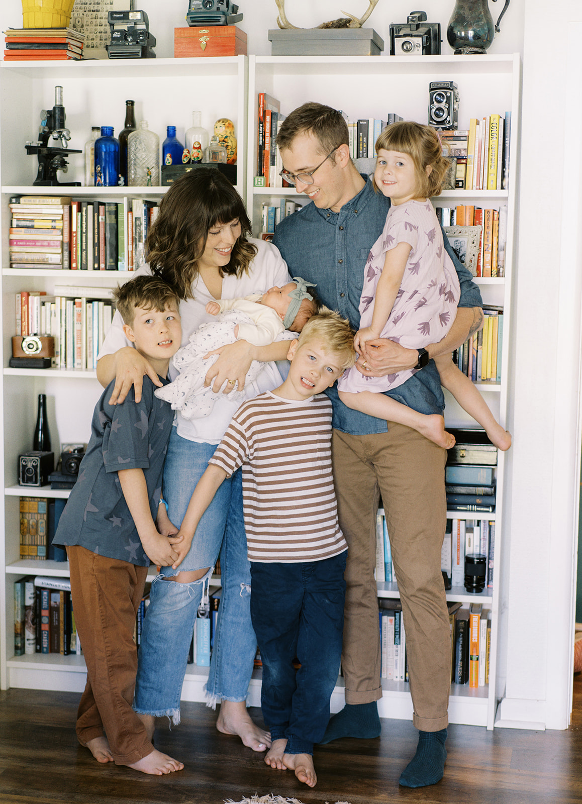 A family of 6 stands in front of a bookshelf with the new baby during their at-home lifestyle session