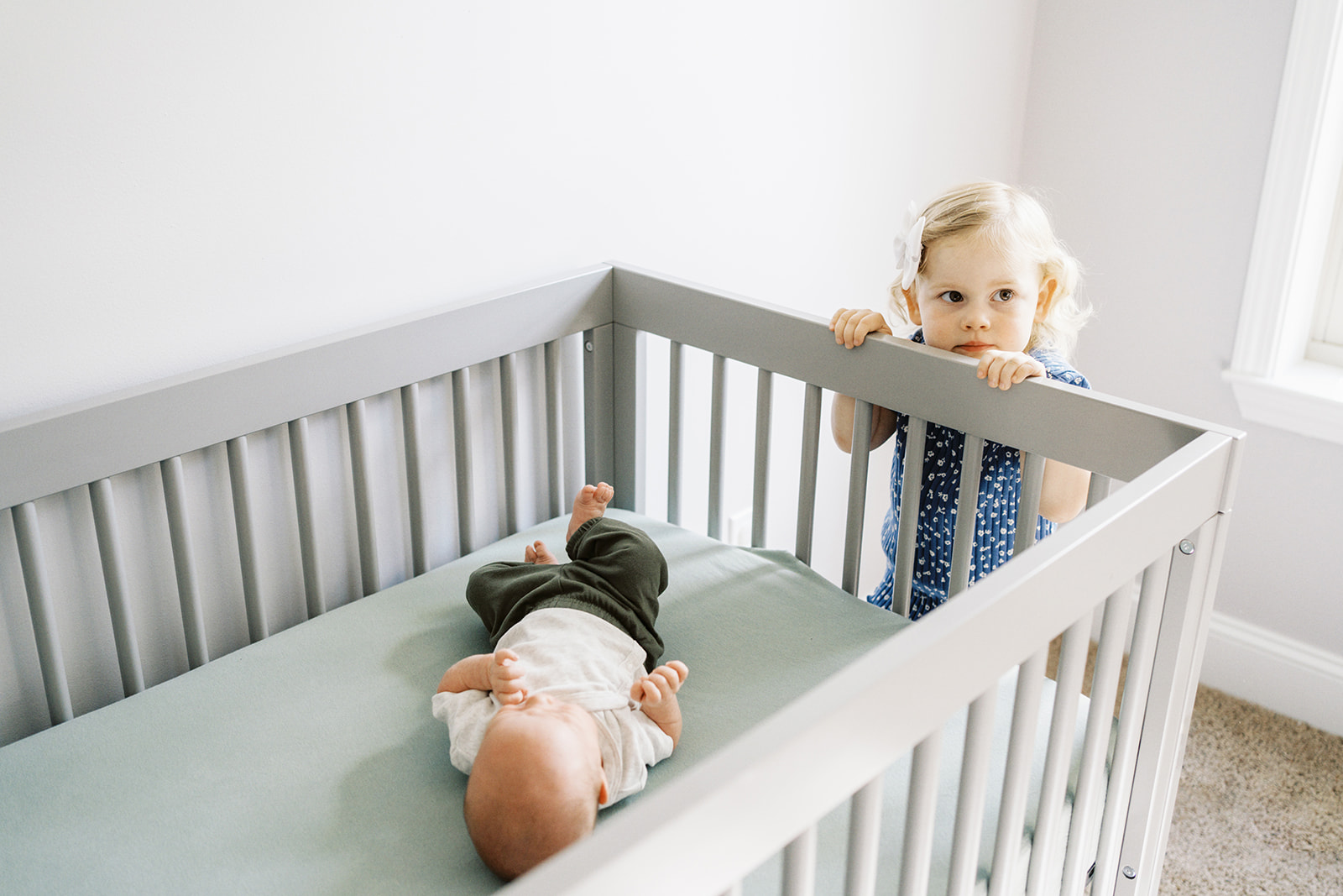 Big sister looks over the crib at her baby brother during a family lifestyle session