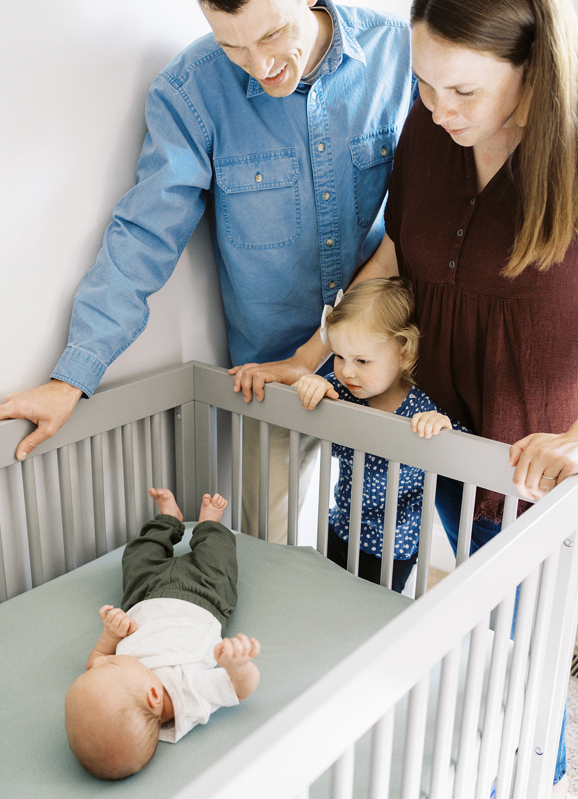 The family looks over the crib at the newborn baby boy during a family lifestyle photography session