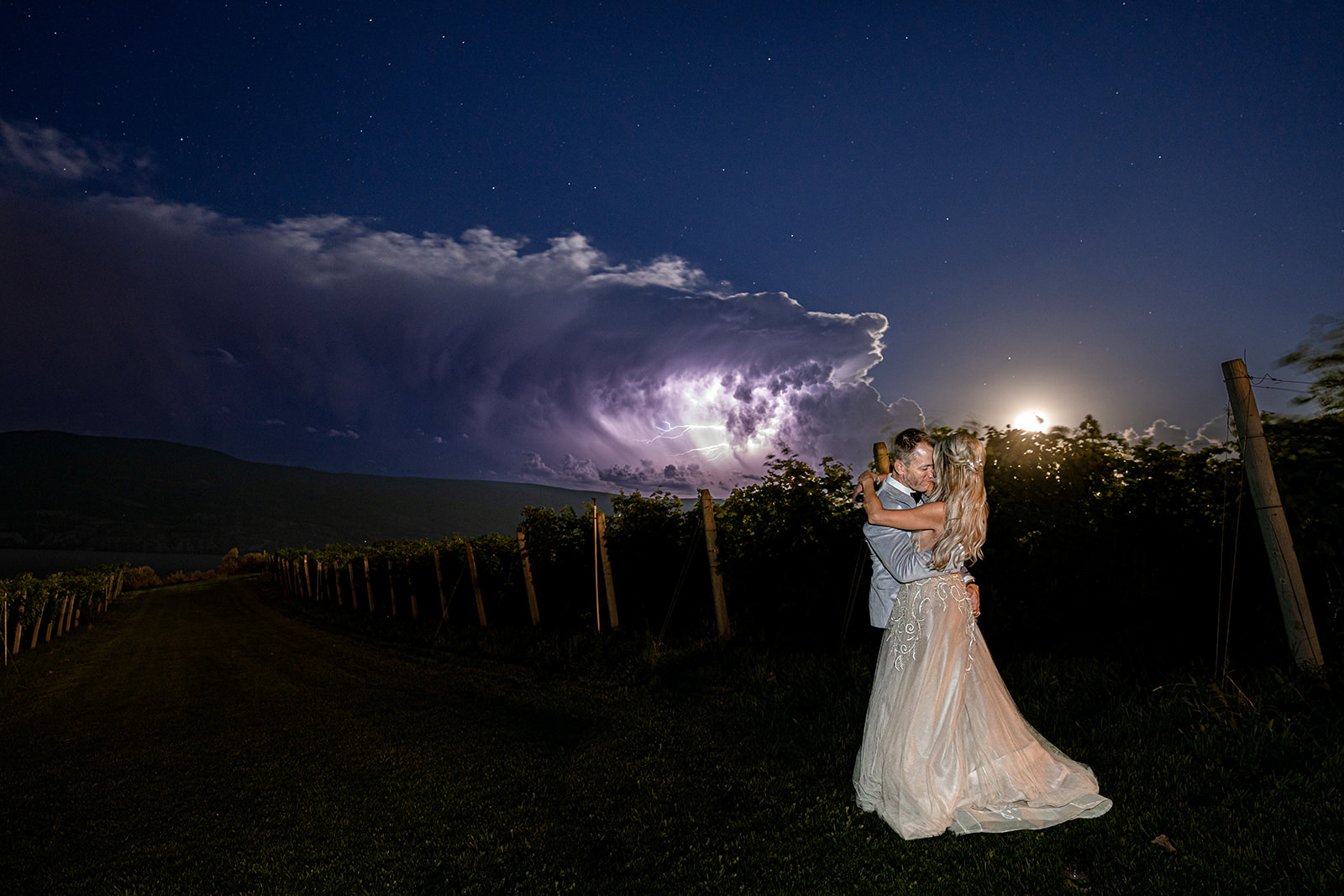 Bride and groom kiss under lightening in the clouds above their Oak Estate Winery wedding.