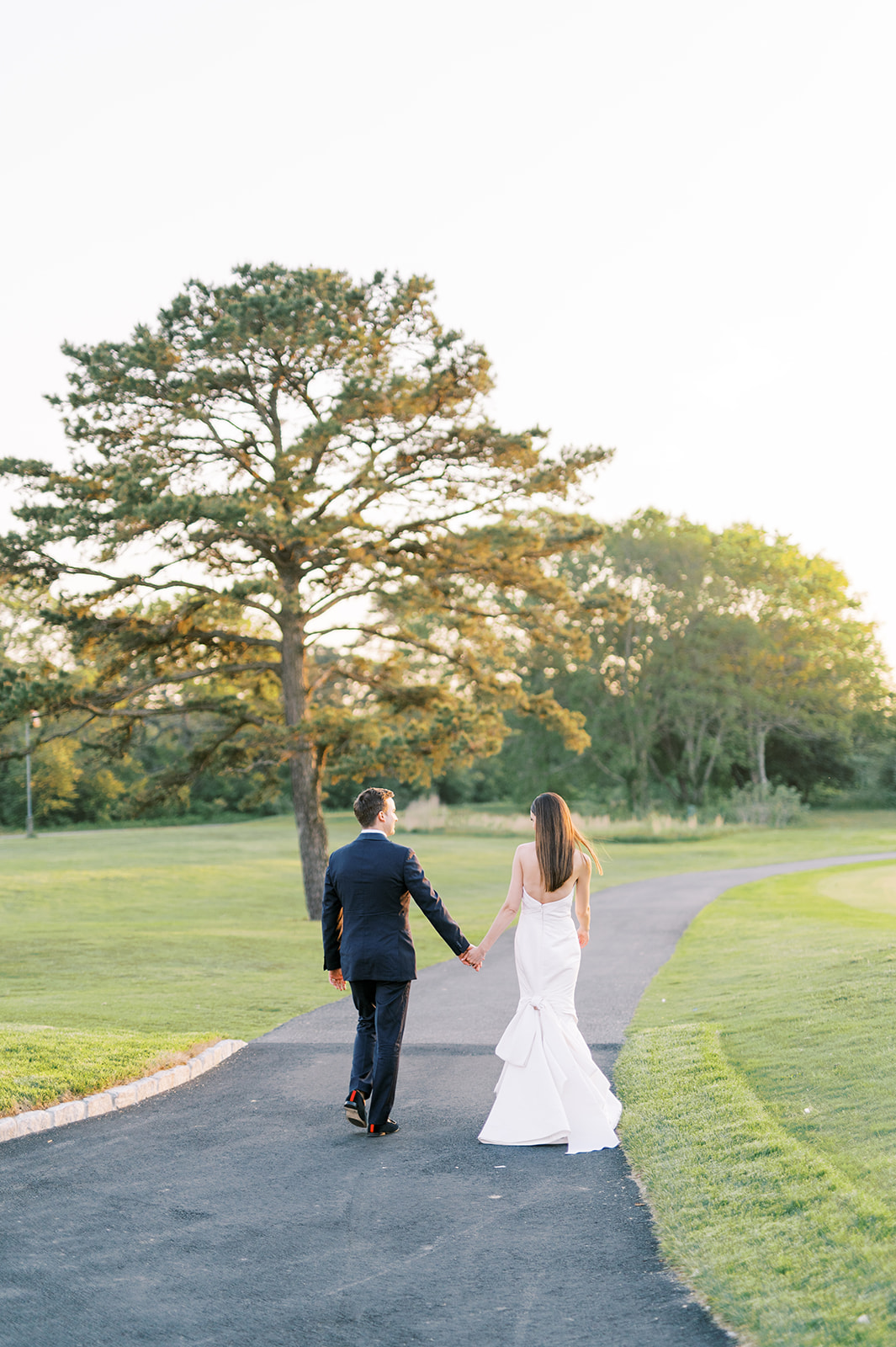 bride and groom hold hands walking during sunset at Bright Summer Stone Harbor Golf Club Wedding in Yellow and Blue