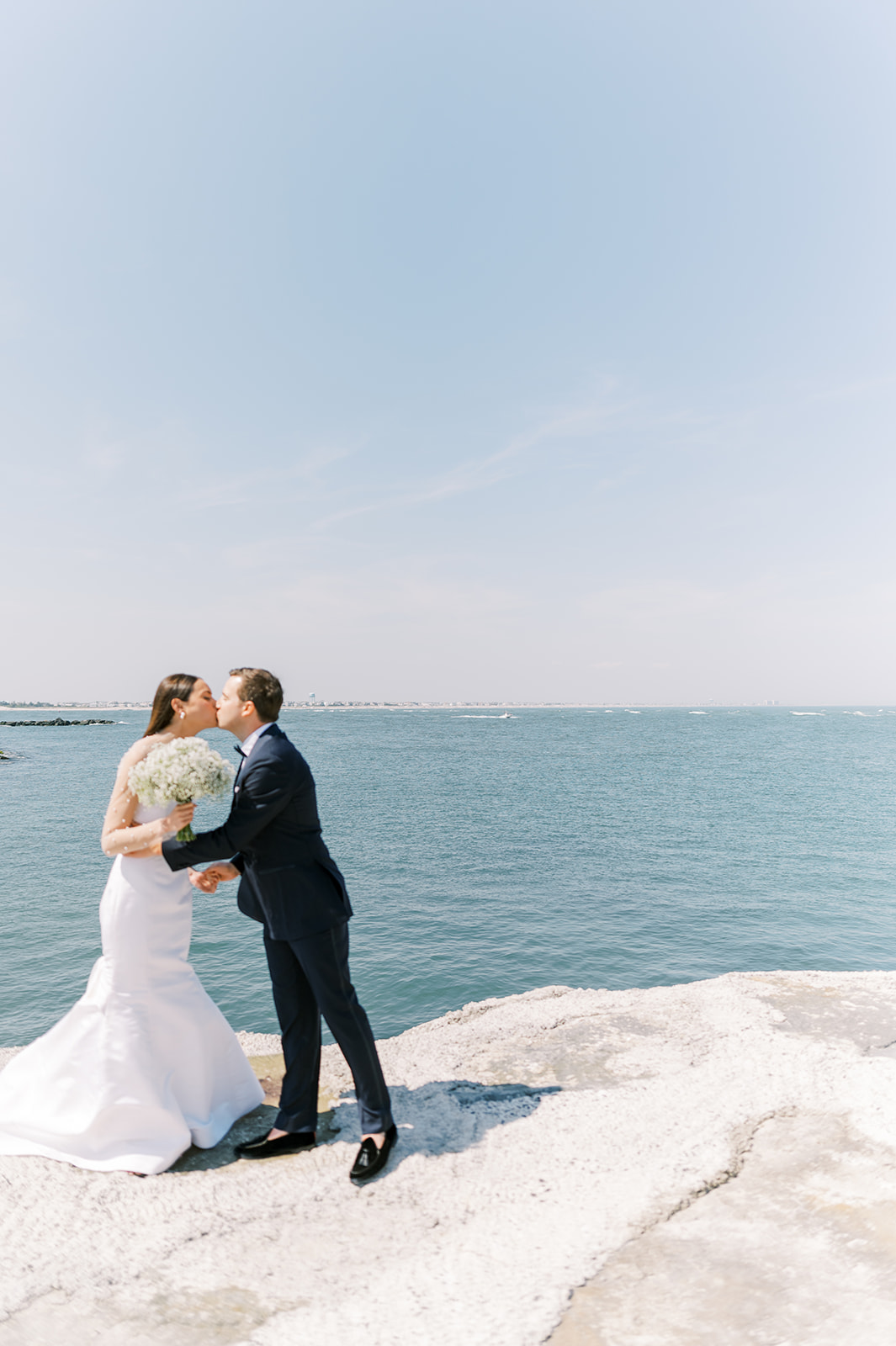 bride and groom kiss in front of the blue ocean for Bright Summer Stone Harbor Golf Club Wedding in Yellow and Blue