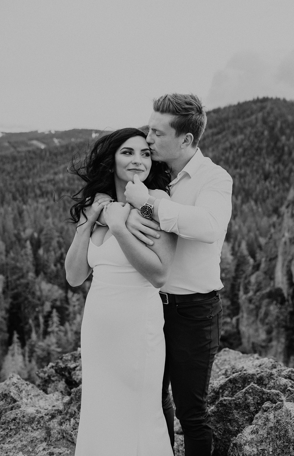 A black and white photo of a mountain top kiss between a couple