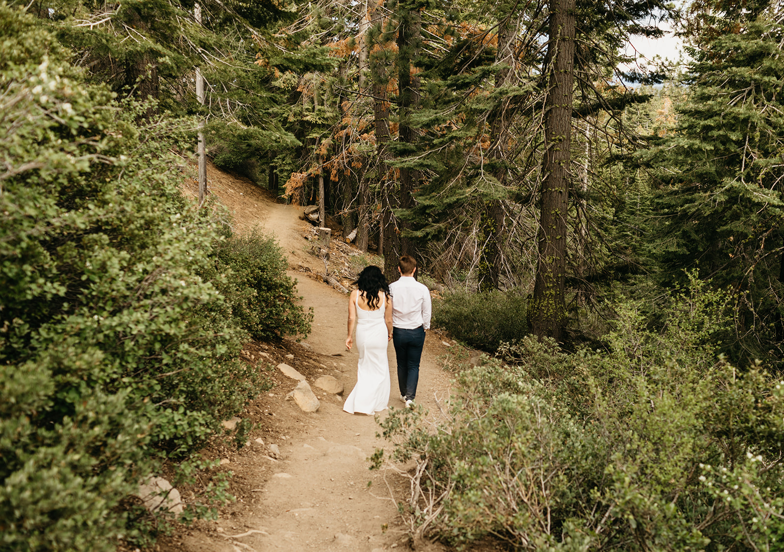 A couple wearing formal attire walk along a trail in tahoe national forest 