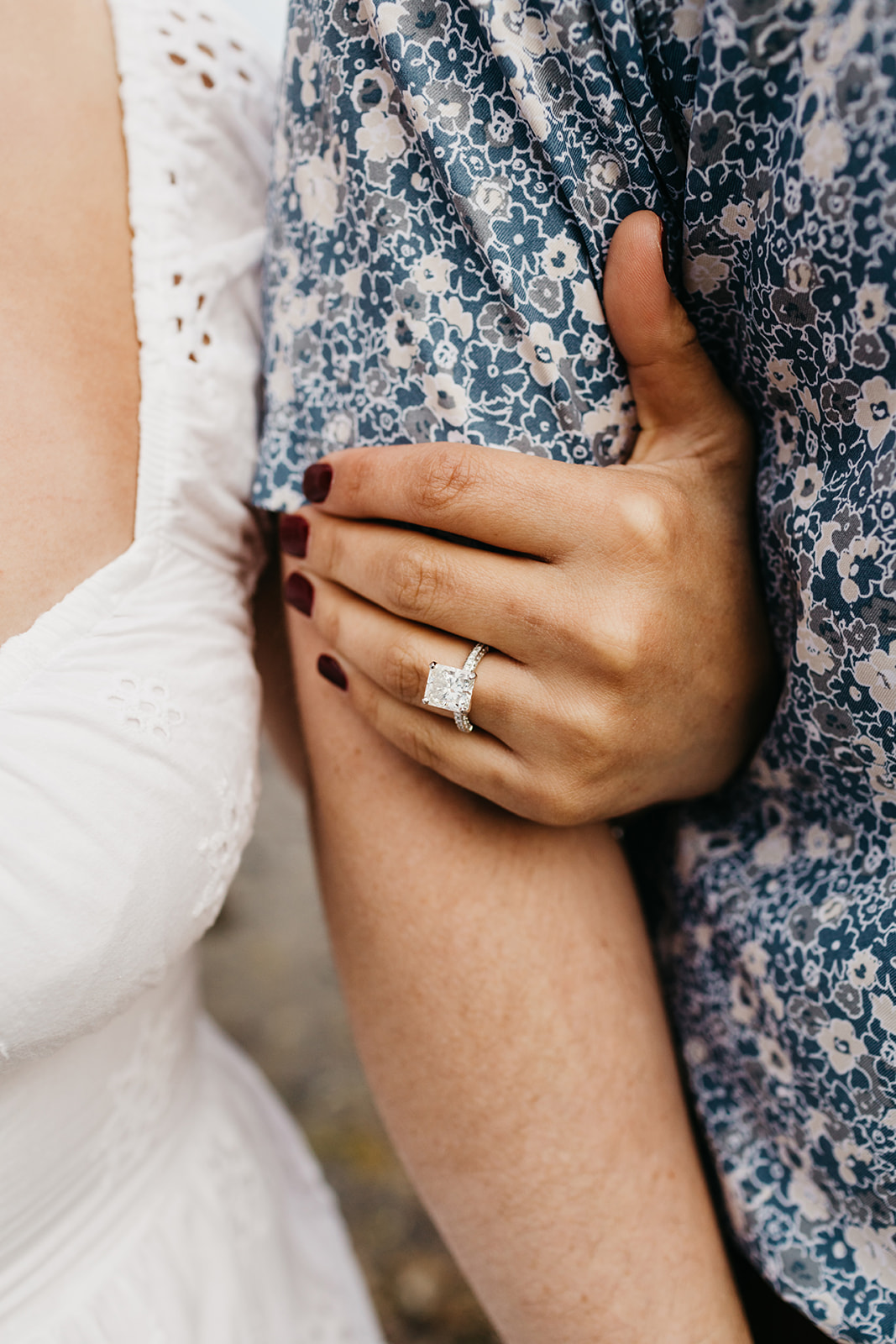 A womans hand wrapped around her fiances bicep showcasing her engagement ring