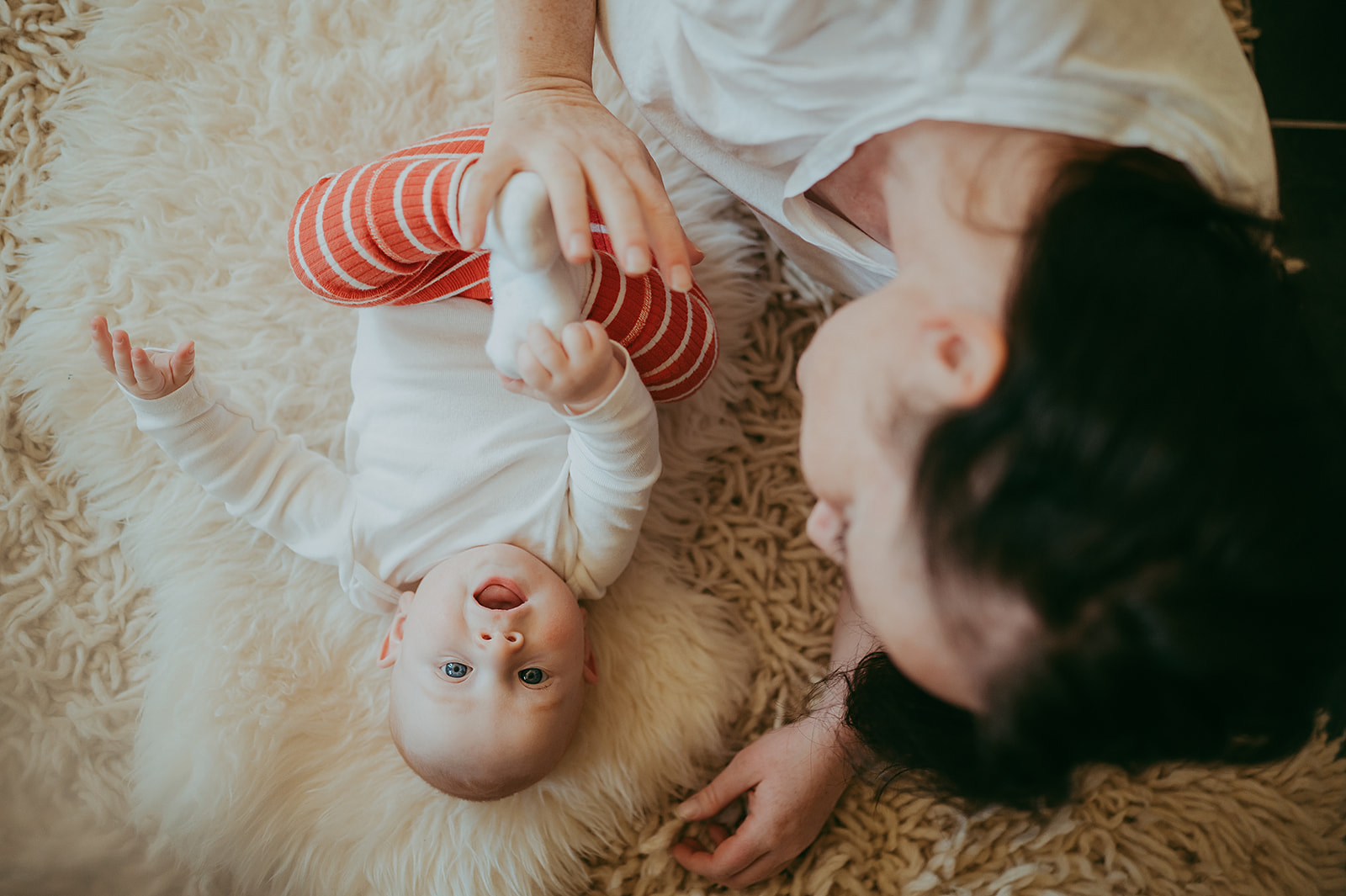 baby laughing on sheepskin rug with mother