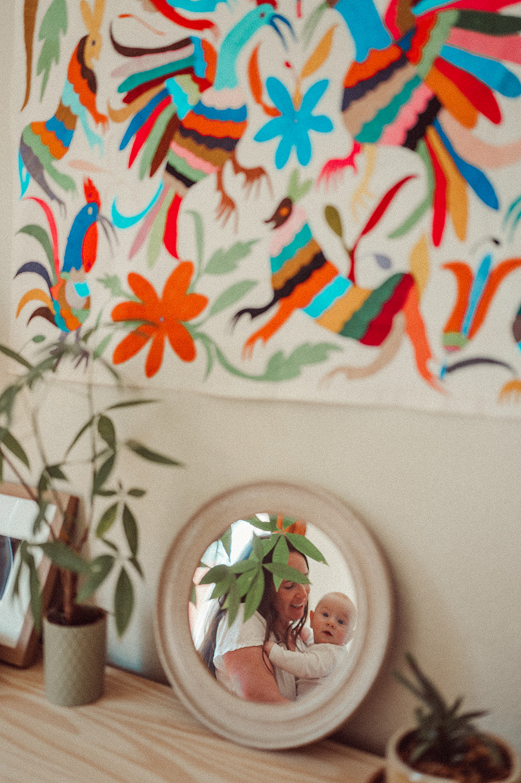 Mother and baby in mirror next to otomi wall hanging