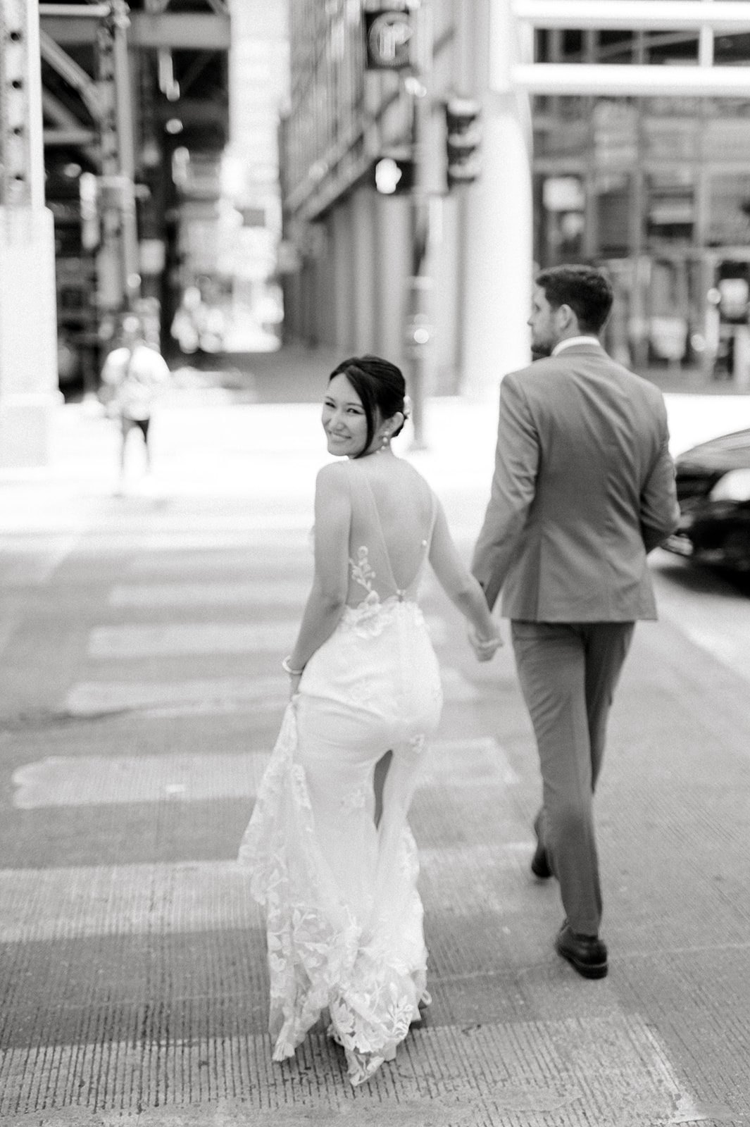 black and white photo of bride and groom walking away down street