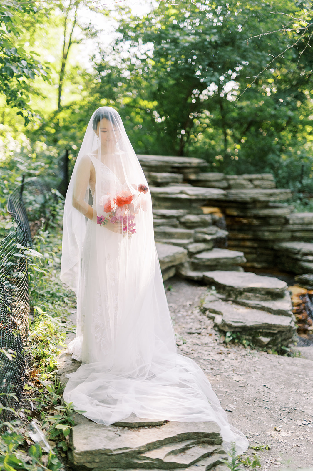 bride with modern bright red bouquet in green setting with veil draped over her