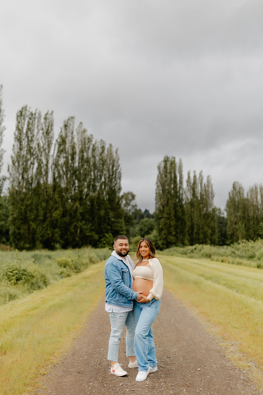 Photo of a young Latino couple posing for a maternity photoshoot in Woodinville, WA, under gloomy skies.