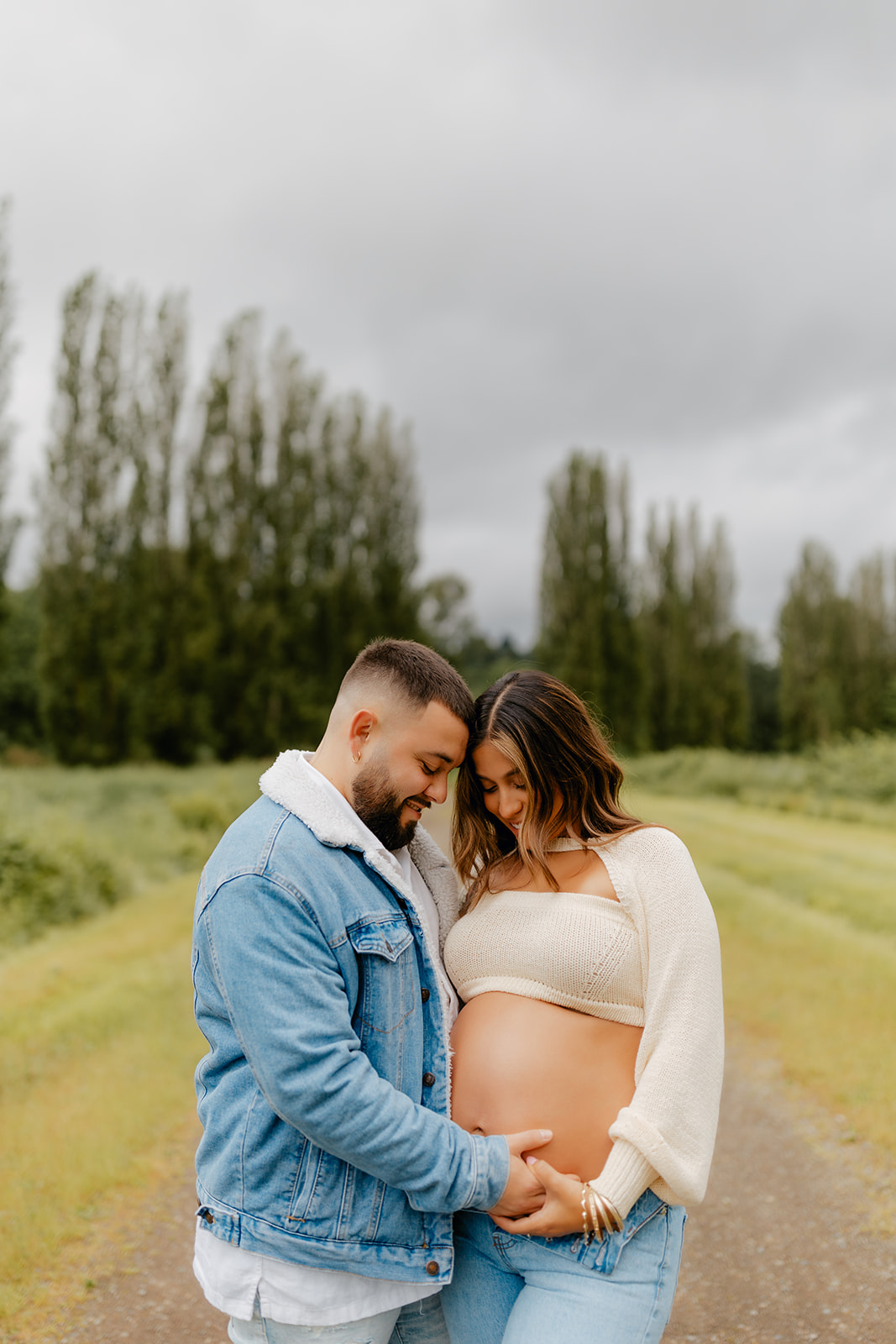 Close-up photo of a young Latino couple posing for a maternity photoshoot in Woodinville, WA, under gloomy skies.