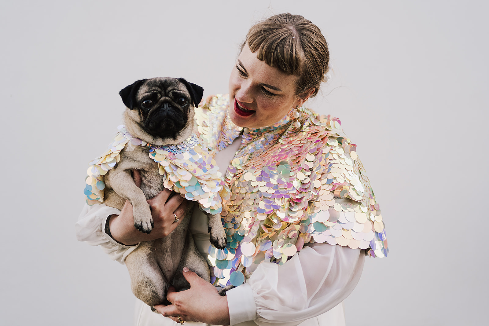 Bride in sequinned cape holding a pug 