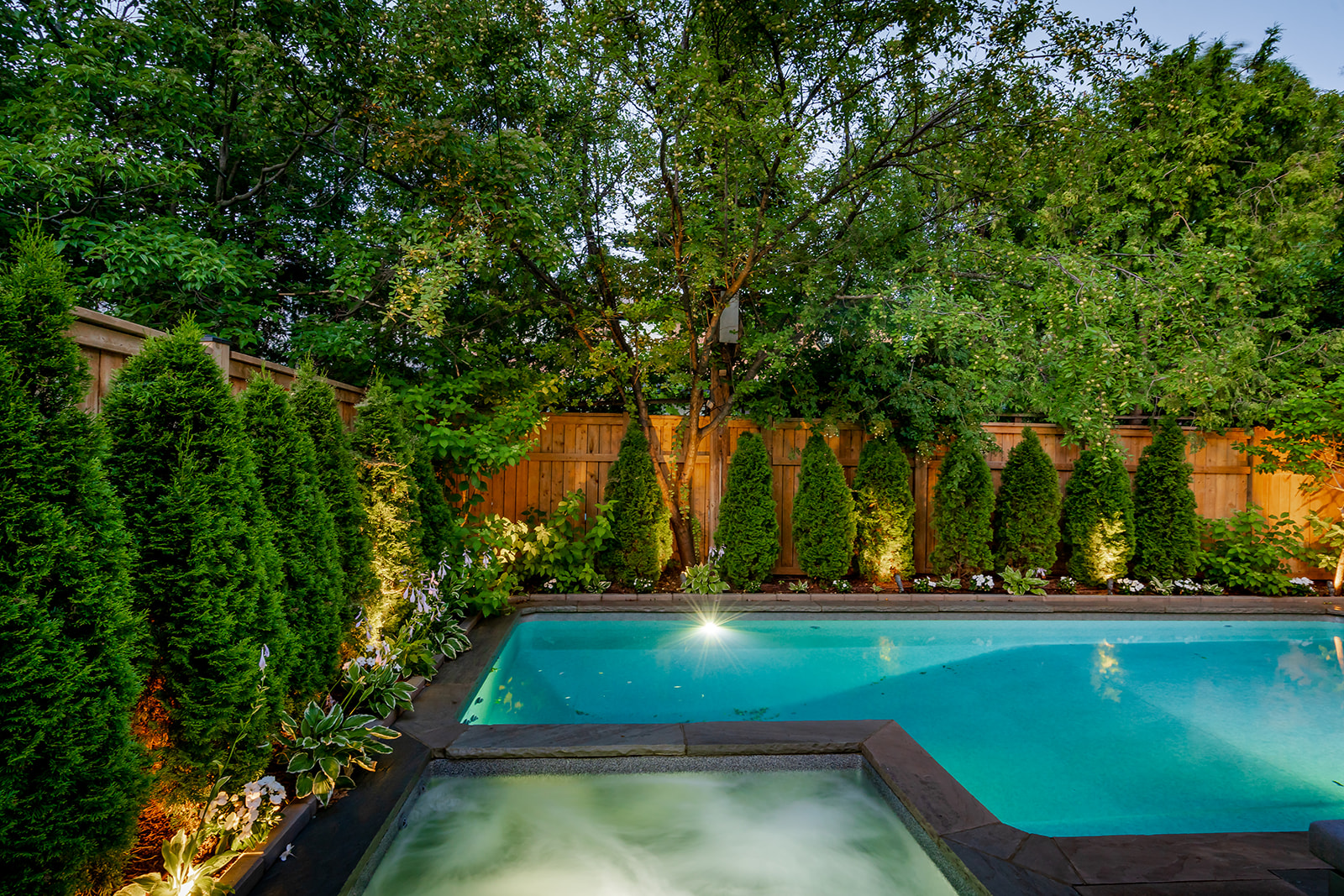 An inground pool with a jacuzzi on the left and trees surrounding the pool.