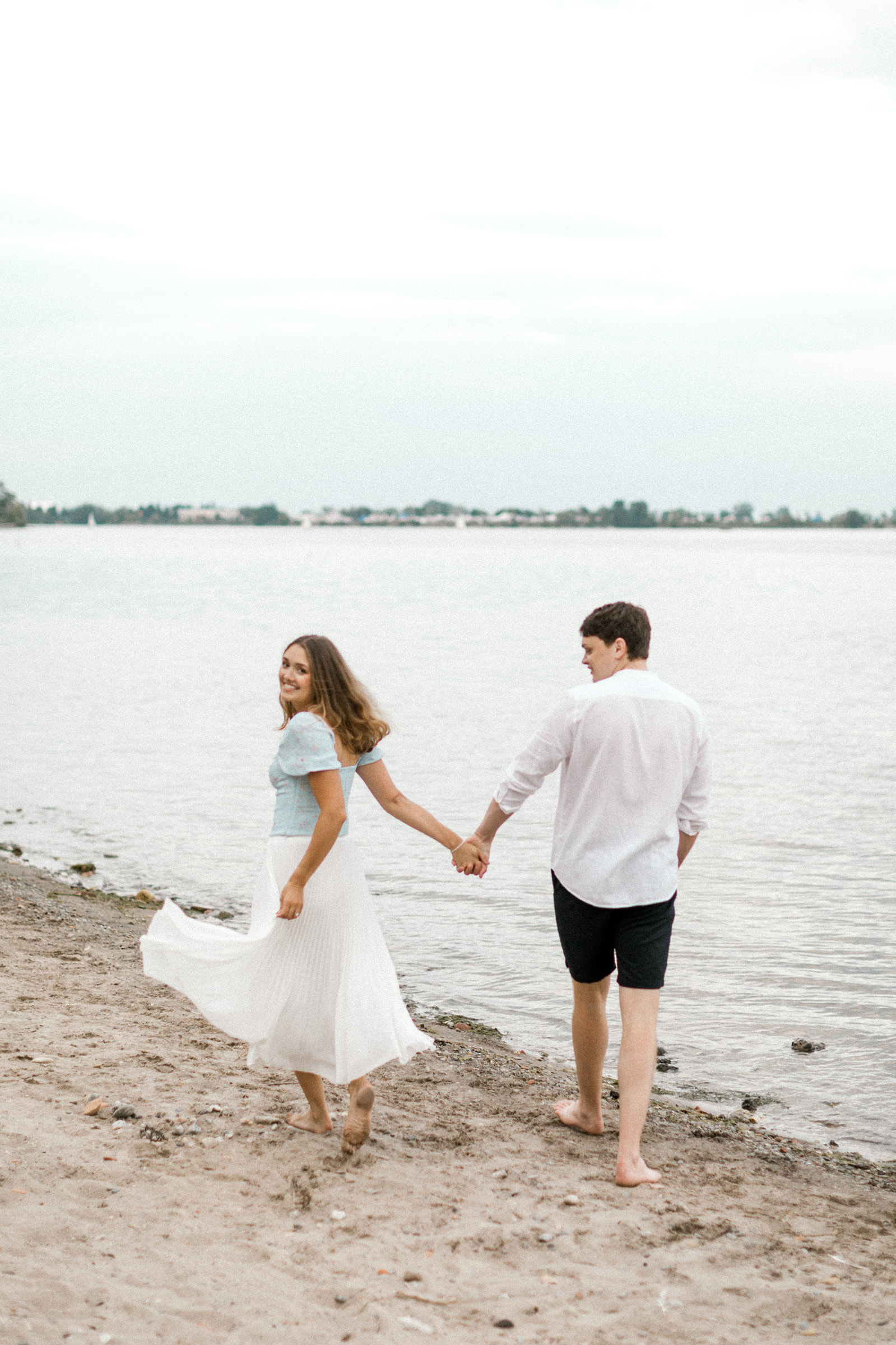 Couple holds hands and runs down the beach during their engagement photoshoot 