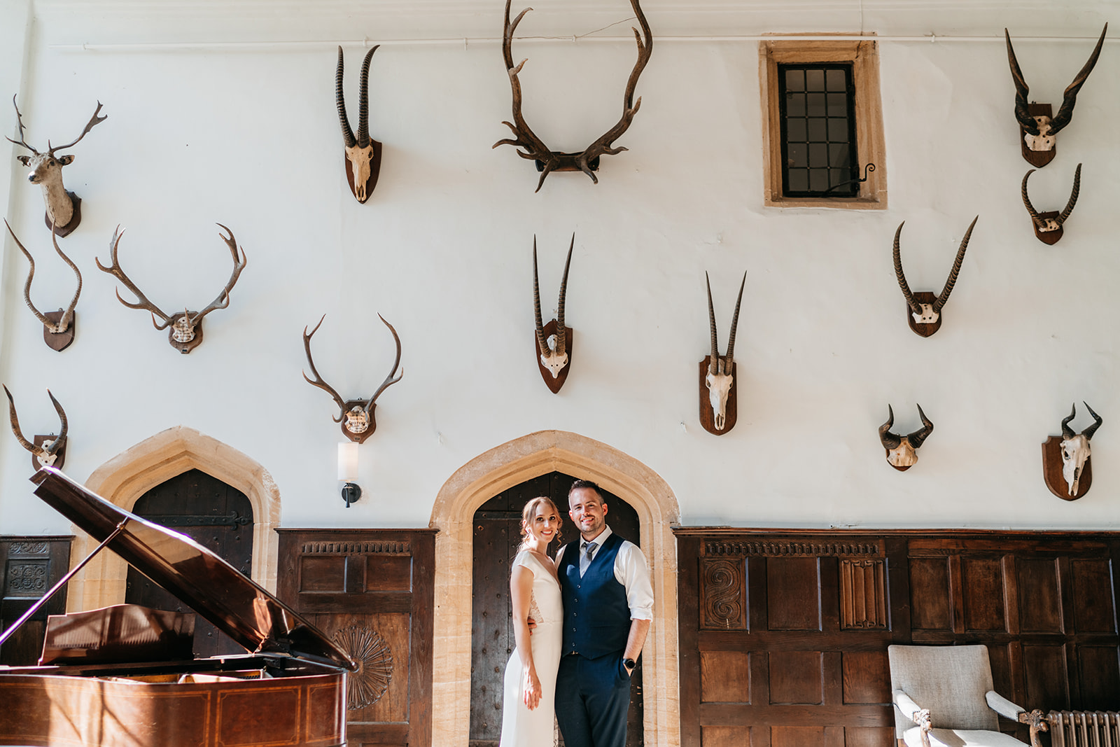 The bride and groom stood underneath the stag heads on the wall of the great hall