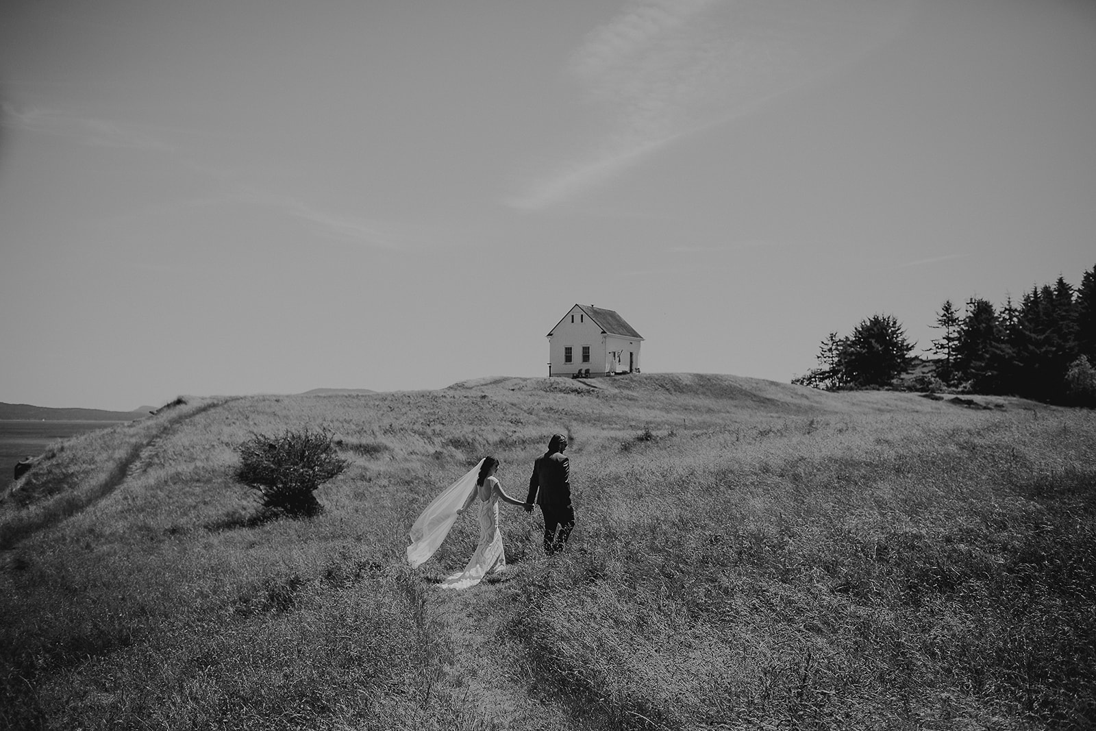 a black and white photograph of a just married couple walking through a field 