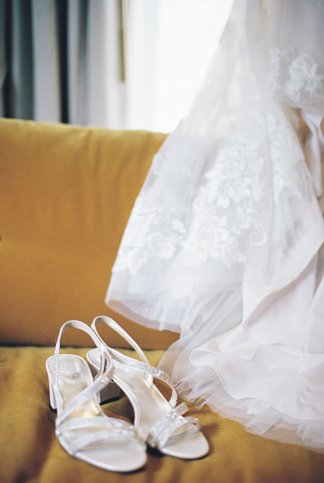 wedding shoes next to white wedding dress on yellow couch