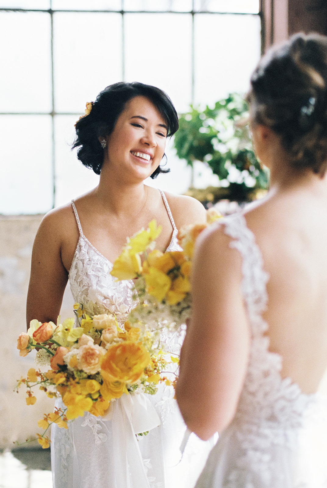 bride holding yellow and orange bouquet smiling at another bride