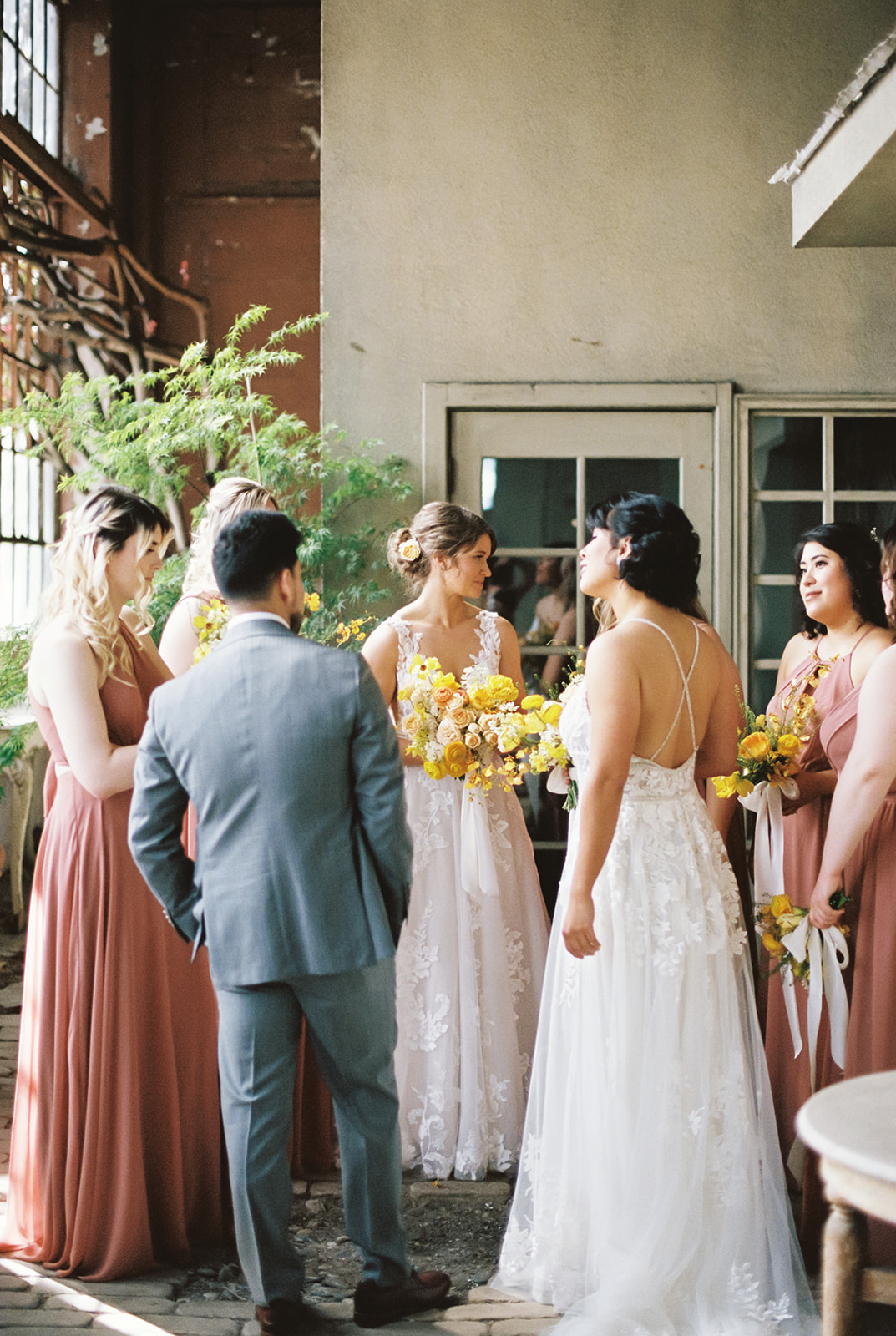 two brides stand laughing with their friends at The Ruins wedding venue