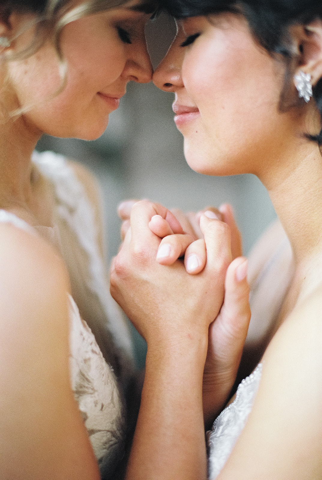 two brides clutch hands between them and snuggle their faces together