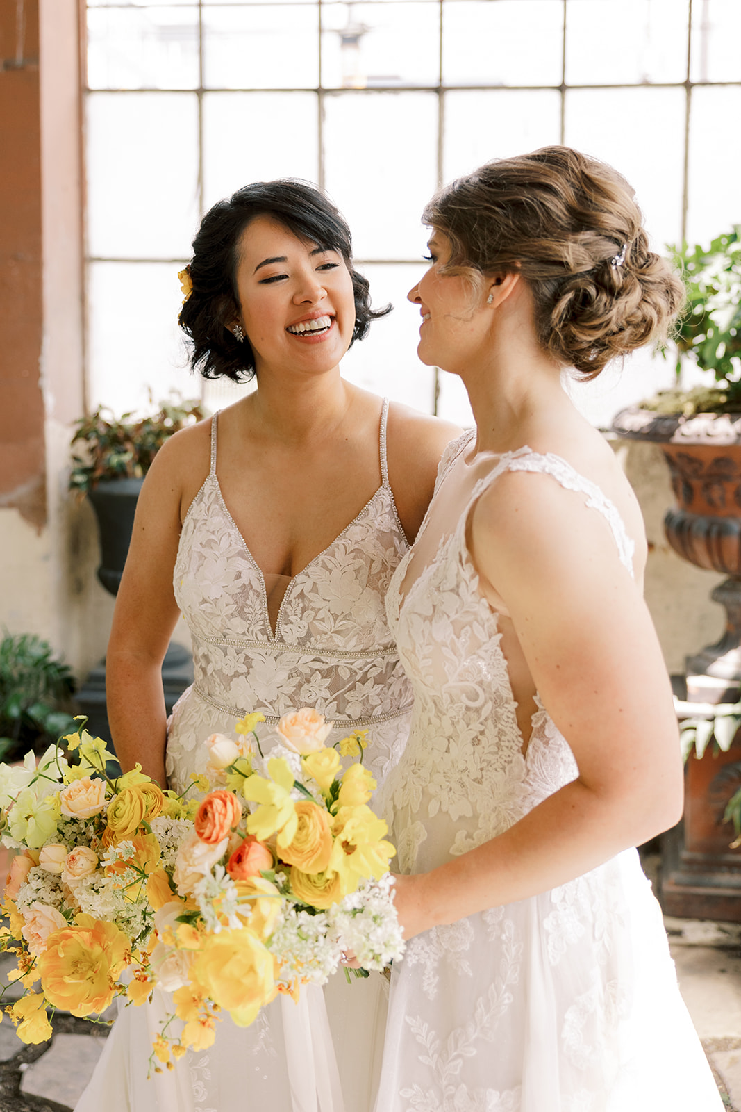 two brides holding orange and yellow bouquets and smiling at each other
