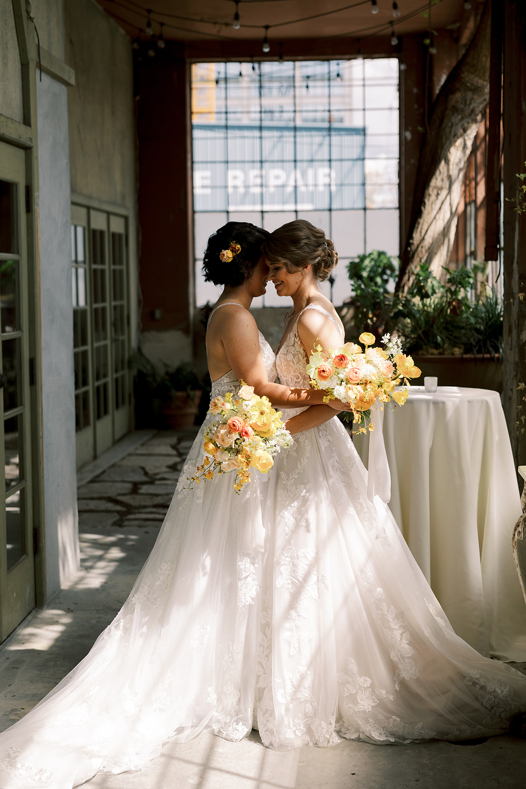 two brides holding each other and touching foreheads holding yellow and orange bouquet