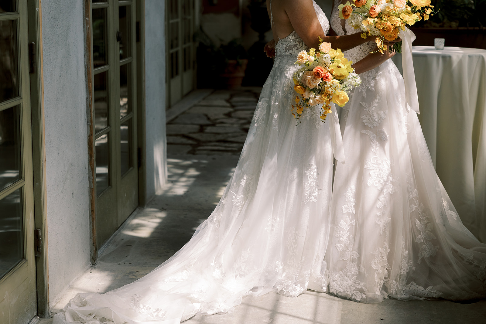two brides holding each other and touching foreheads holding yellow and orange bouquet