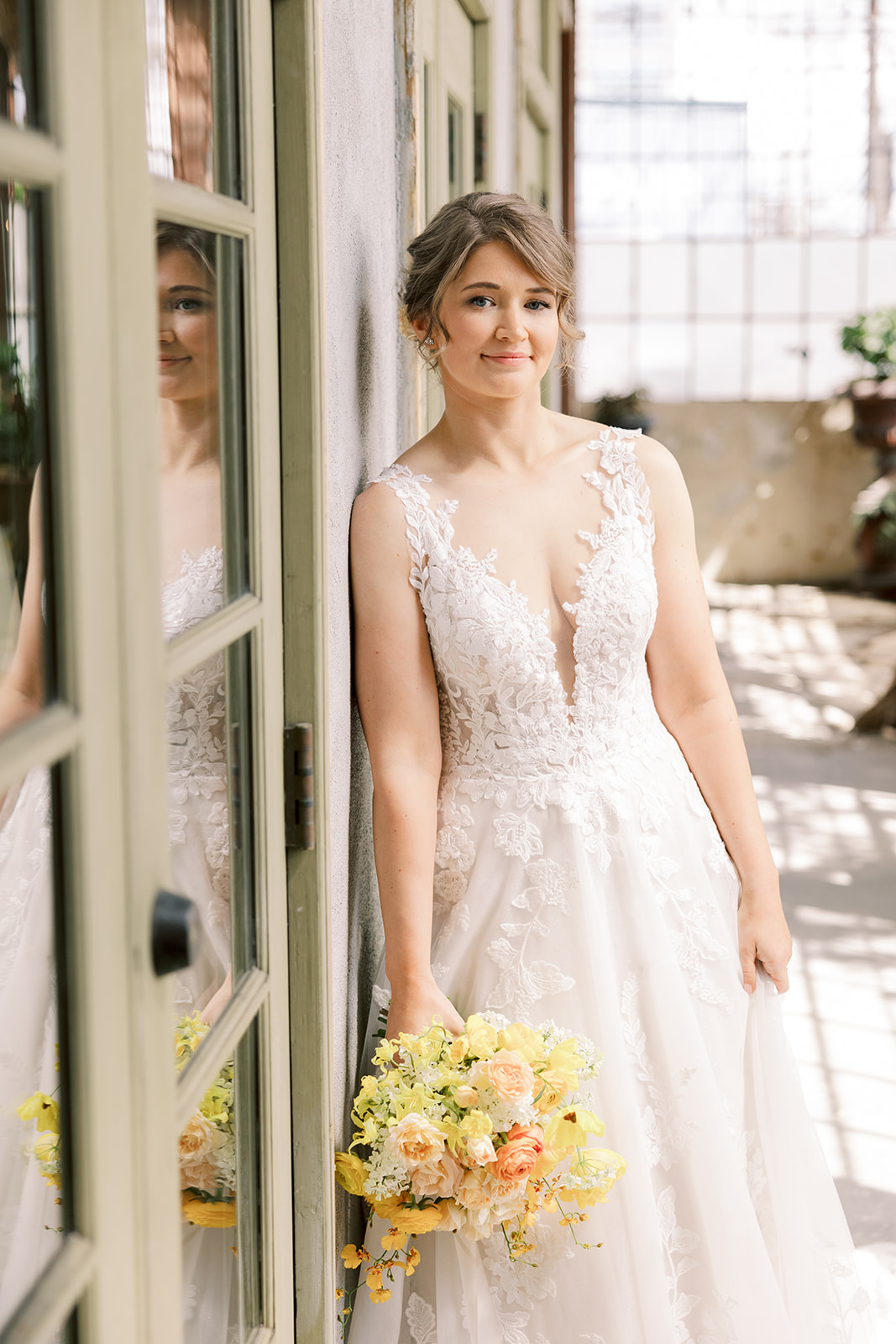 bride leans against wall holding a yellow and orange bouquet