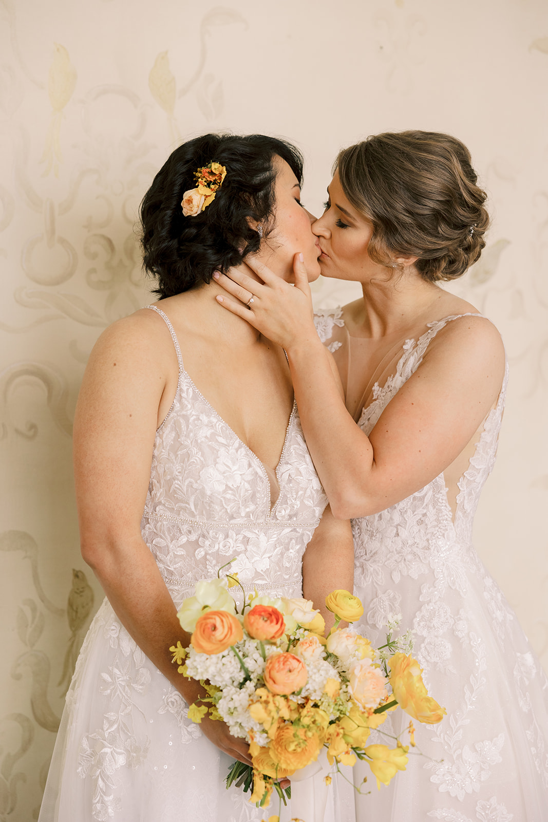 two brides kissing holding orange and yellow bouquet