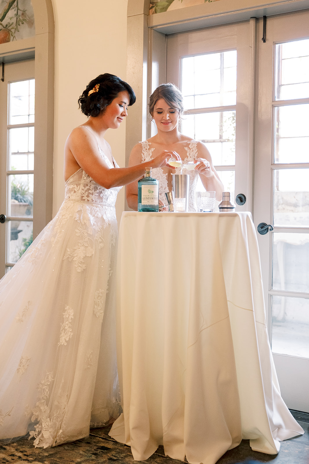 two brides stand at a cocktail table making cocktail