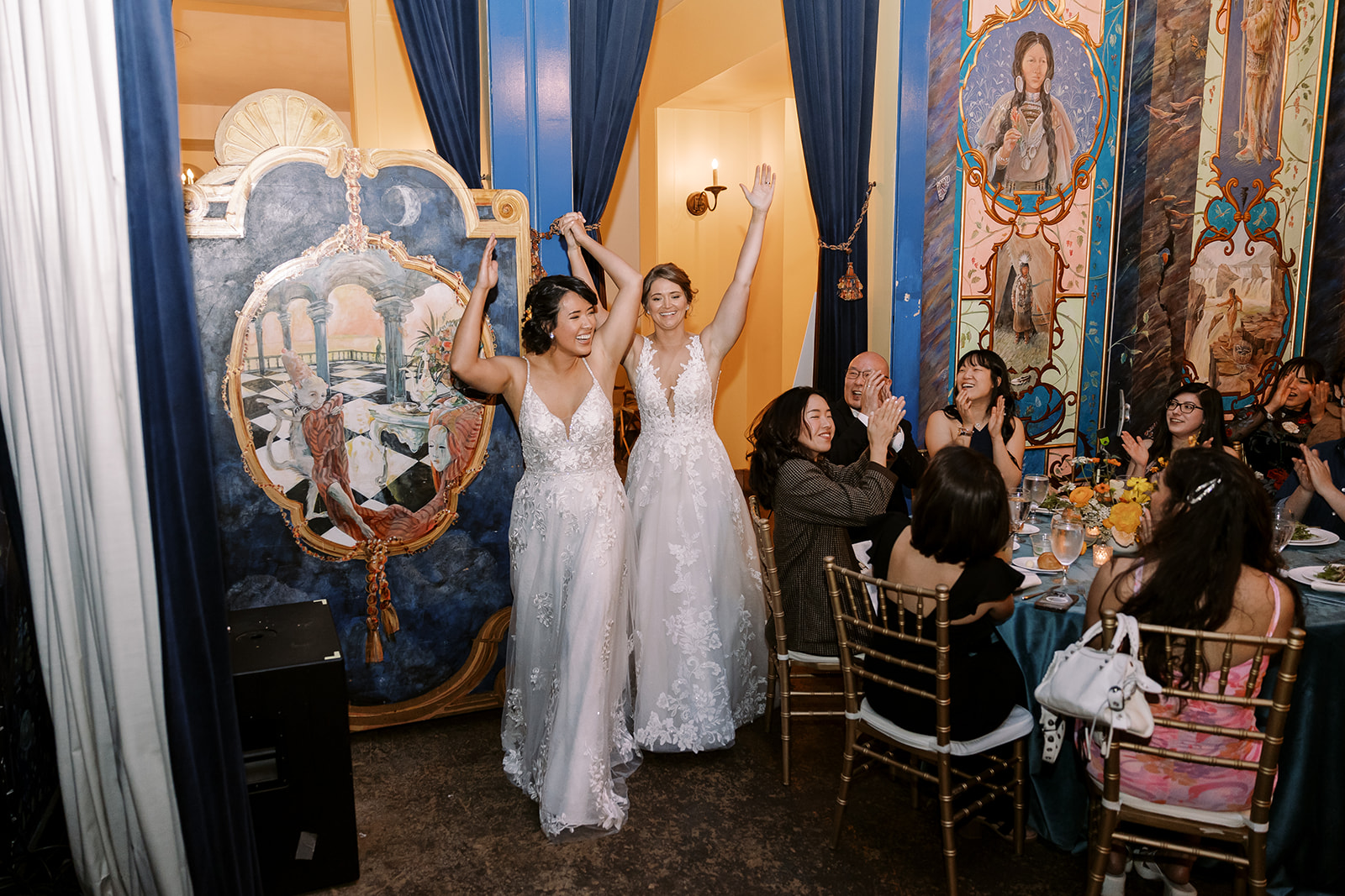 two brides enter reception, arms raised in cheer