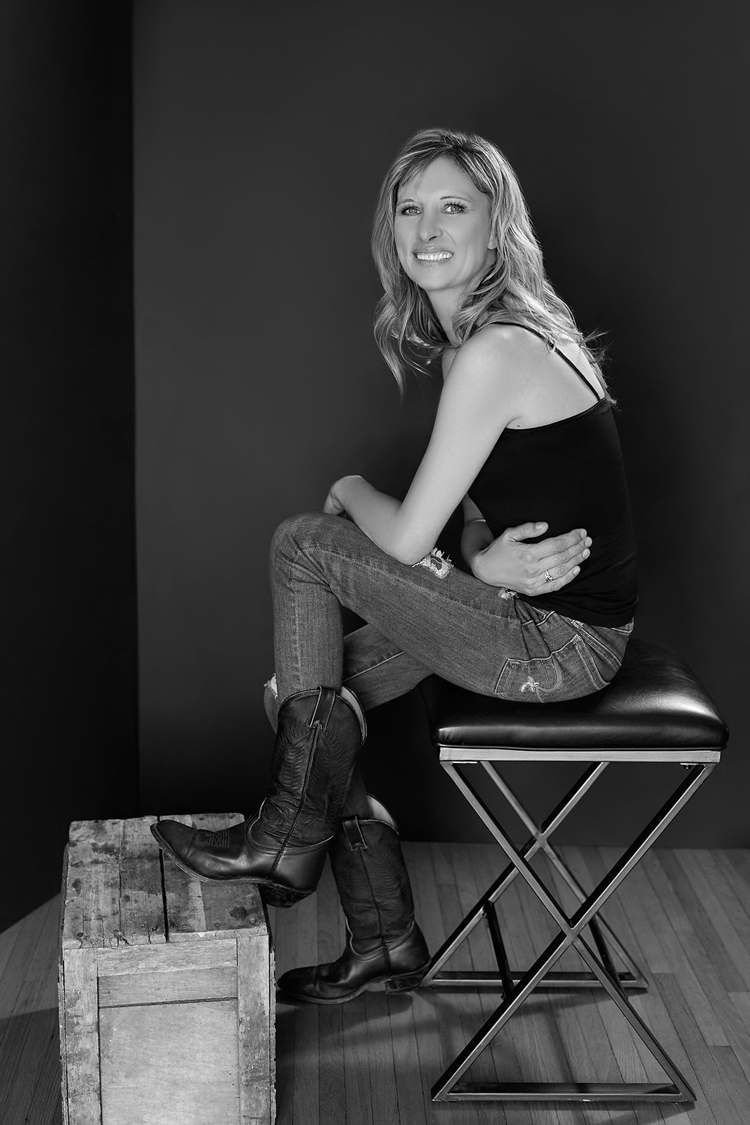 Woman sitting on stool with legs up wearing cowboy boots and looking at camera