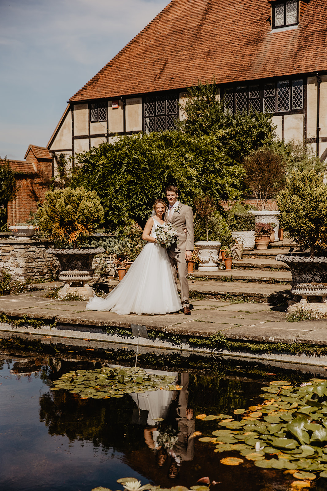 Bride and groom beside still waters at a RHS Gardens Wisley Wedding. By Olive Joy Photography