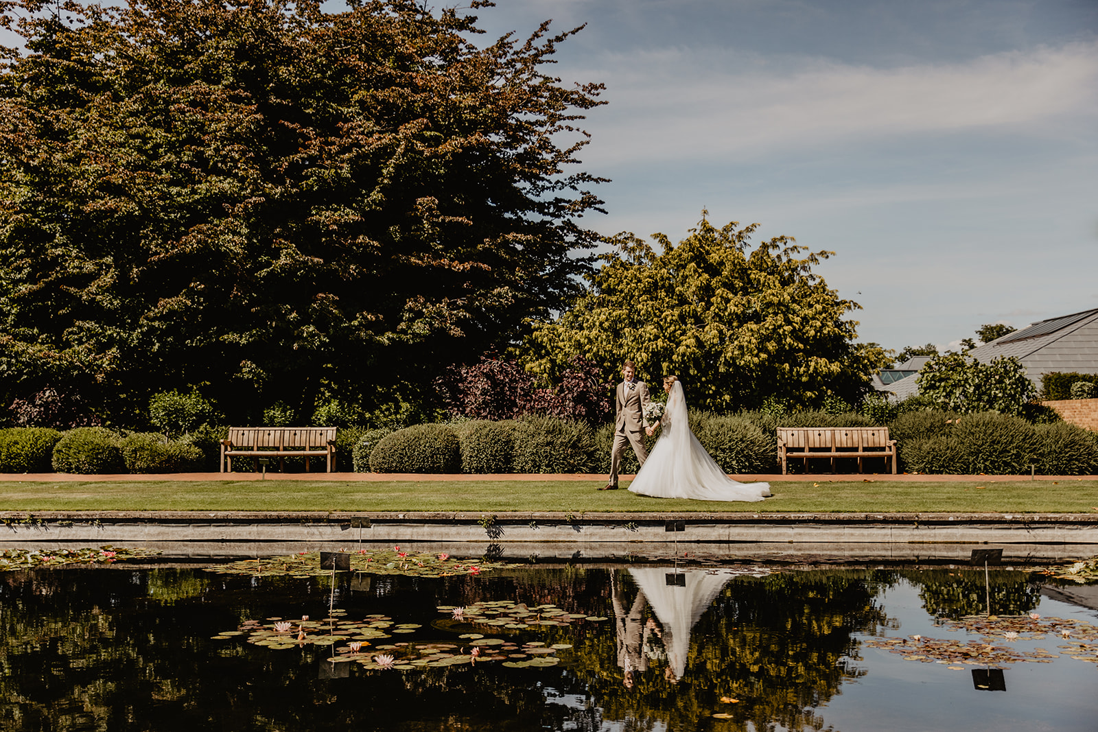 Bride and groom beside still waters at a RHS Gardens Wisley Wedding. By Olive Joy Photography