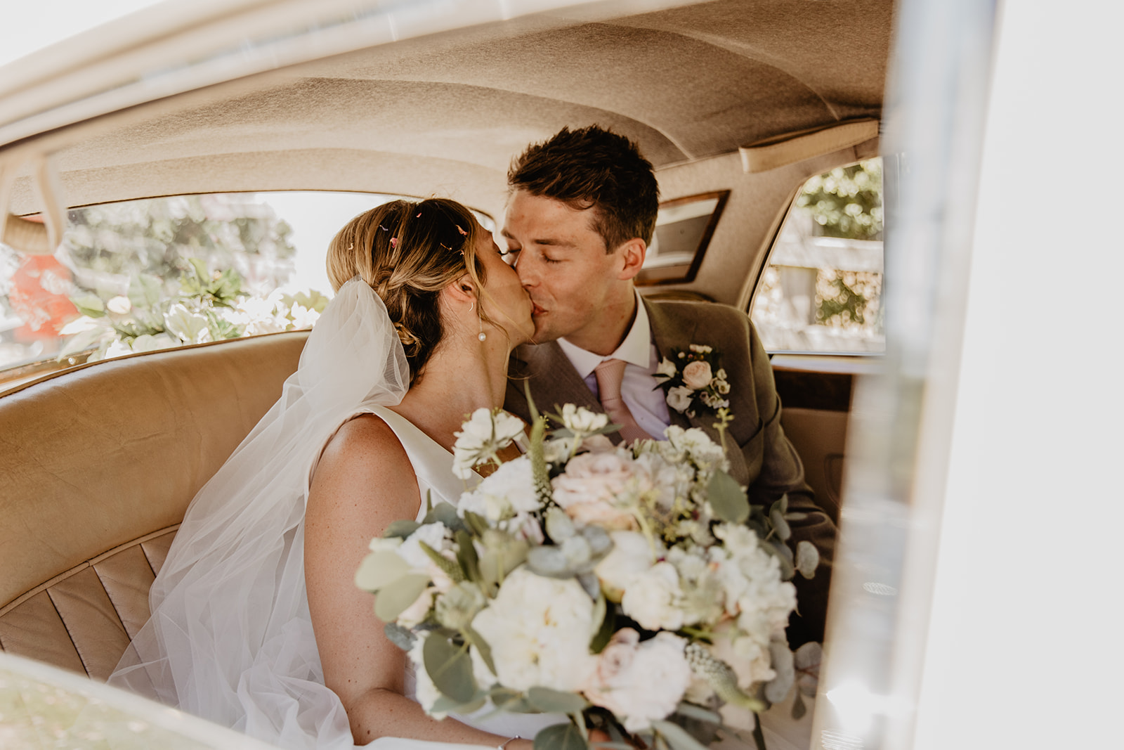 Bride and groom kissing in their wedding car at an RHS Gardens Wisley Wedding. By Olive Joy Photography