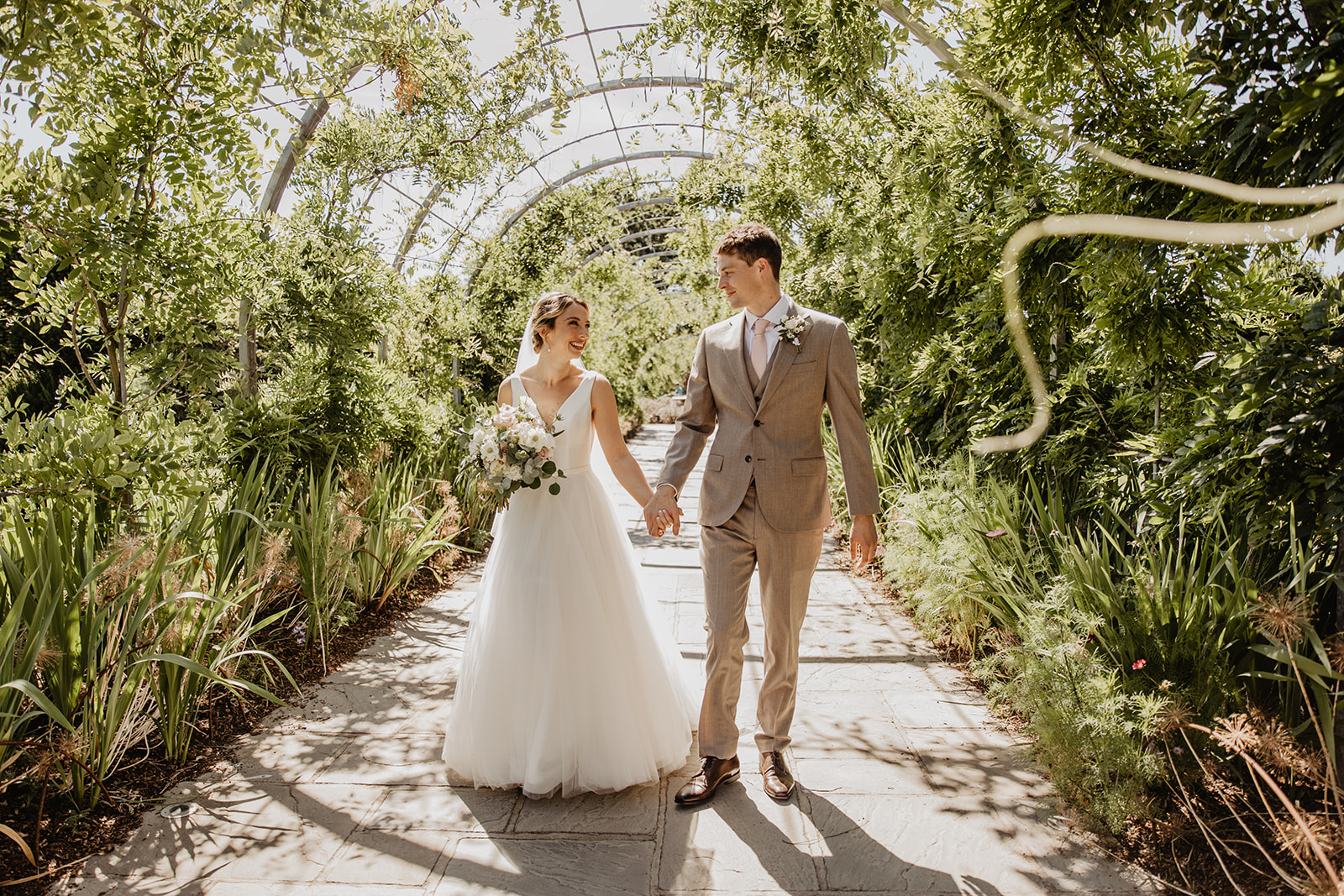 Bride and groom walk through floral archway at a RHS Gardens Wisley Wedding. By Olive Joy Photography