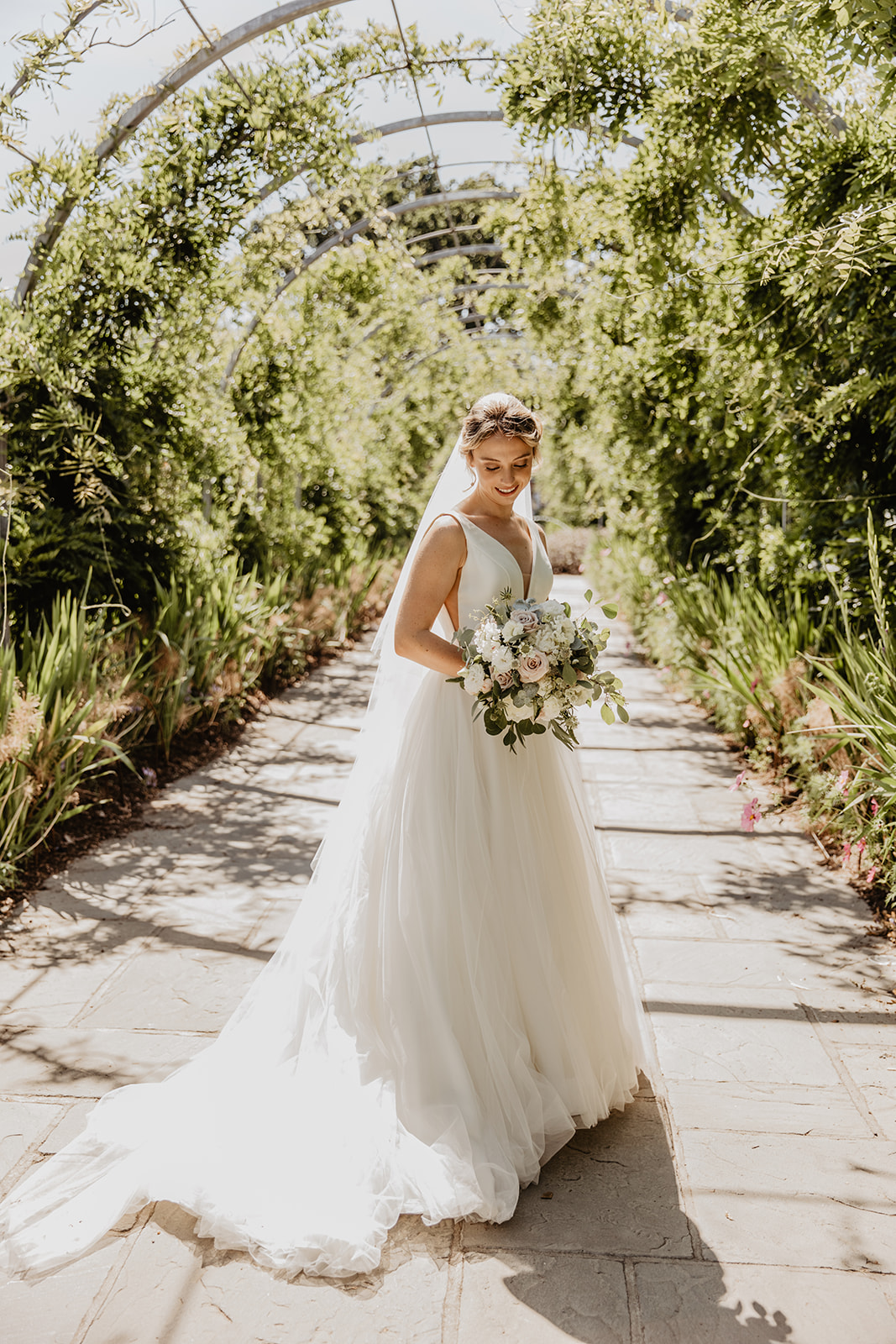 Bride walks through floral archway at a RHS Gardens Wisley Wedding. By Olive Joy Photography