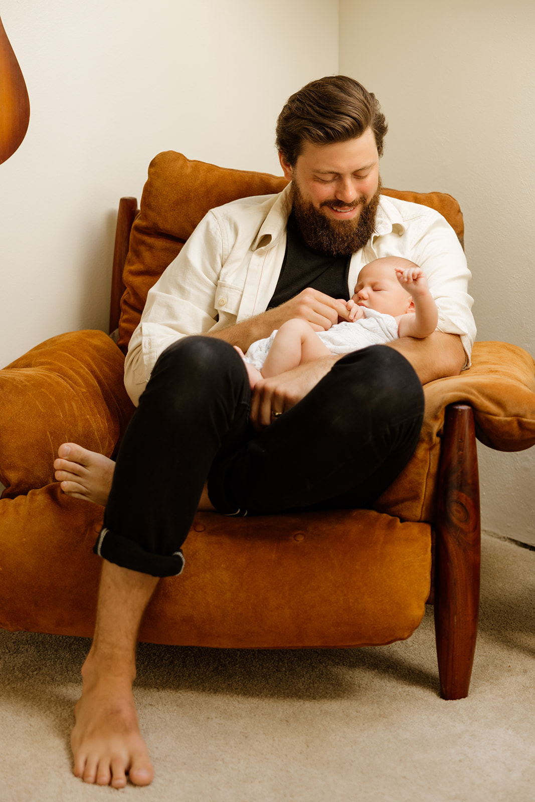 Intimate photo of a father holding his newborn baby while sitting in a comfy chair.