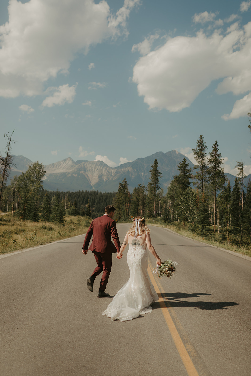 Bride and groom running on road in the mountains near Jasper, Alberta. 