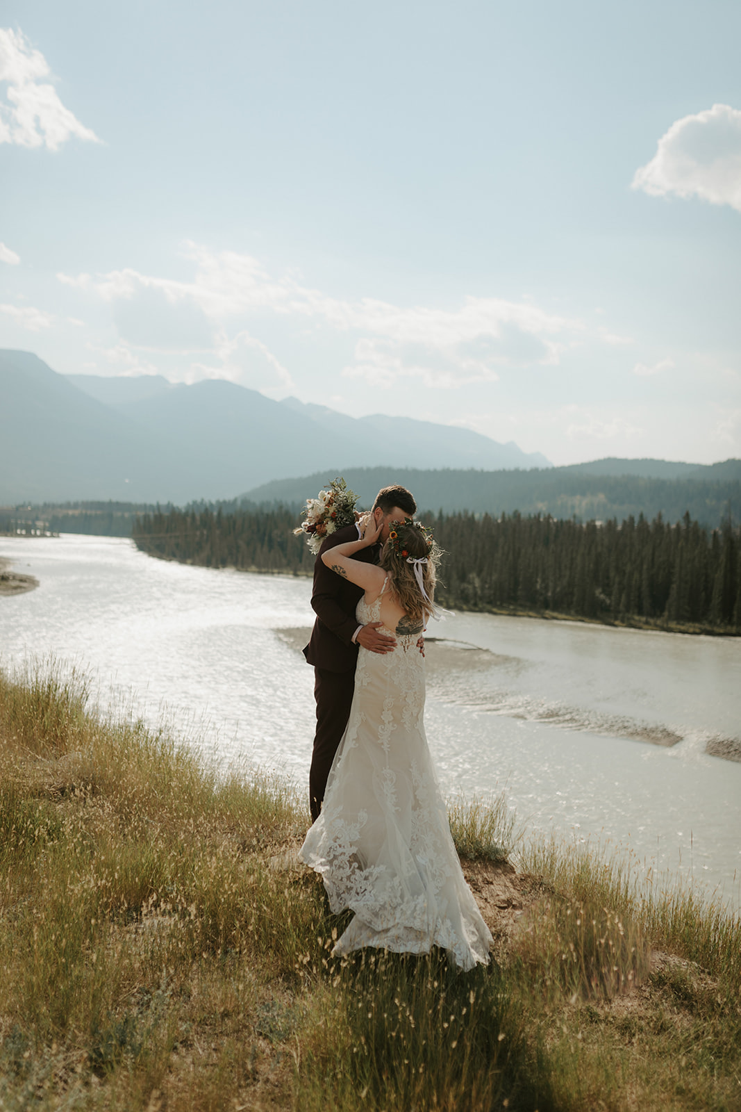 Bride and groom embracing with a mountain landscape in the background alongside the Athabasca Rive in Jasper, Alberta