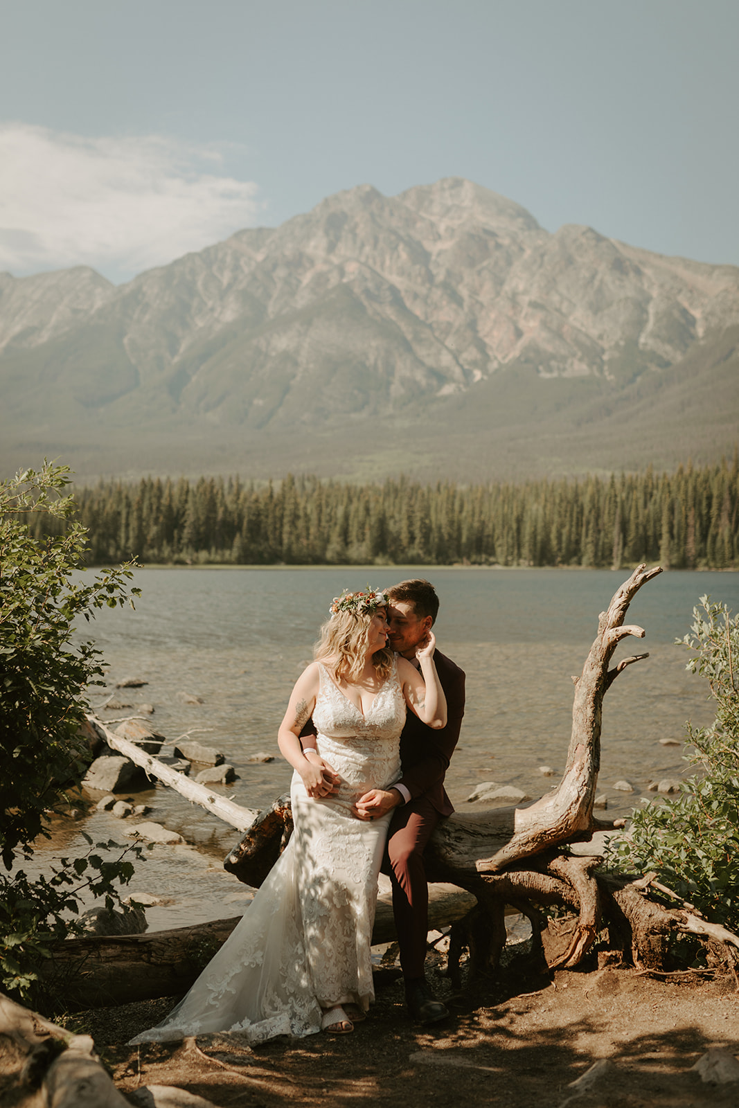Bride and groom sitting on driftwood near Pyramid Lake in Jasper, Alberta
