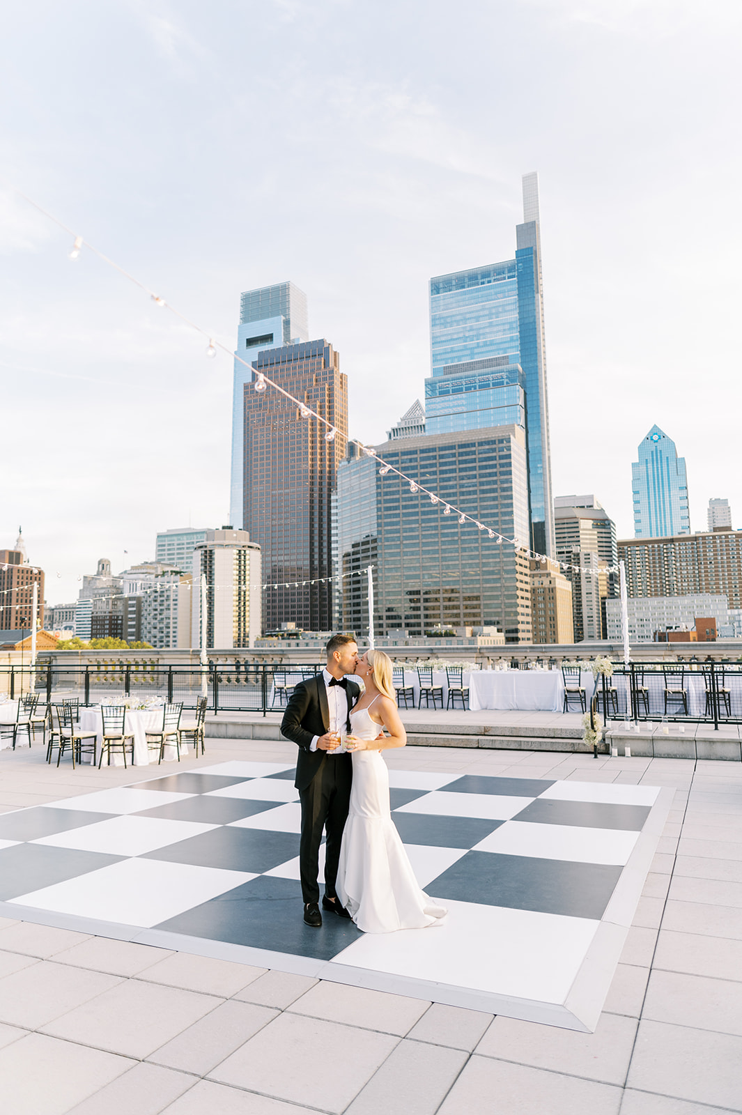 bride and groom kiss in front of city skyline on white checkered dance floor at Free Library of Philadelphia