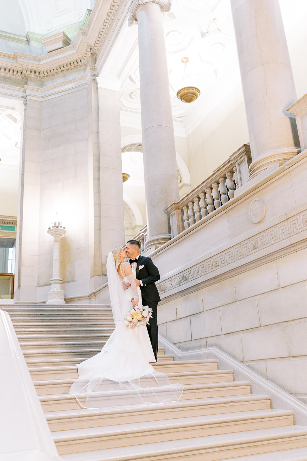 bride and groom kiss on the indoor staircase of the Free Library of Philadelphia for their chic summer wedding 