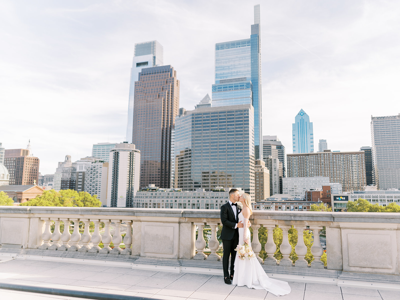chic bride and groom kiss in front of the city skyline on a rooftop for their chic sunny summer wedding day