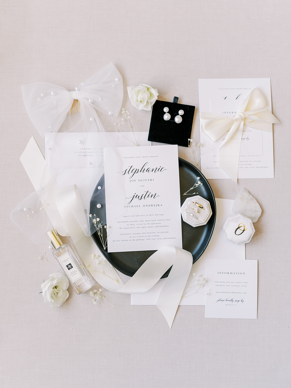 white and black wedding invitations laid out on linen with pearl accents