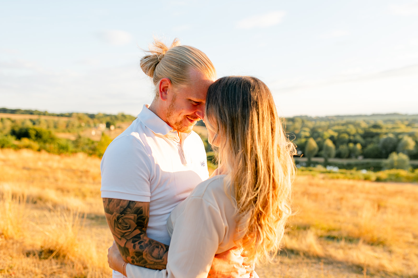 A couple standing facing one another, touching foreheads and arms wrapped around each other in gorgeous golden hour.